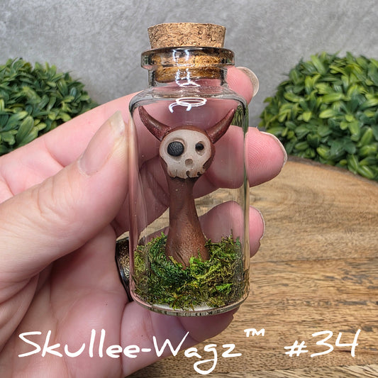 Hand holding a skull faced creature in a jar against a wood background with greenery