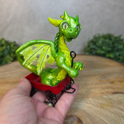 Hand holding a green clay dragon in a red wagon