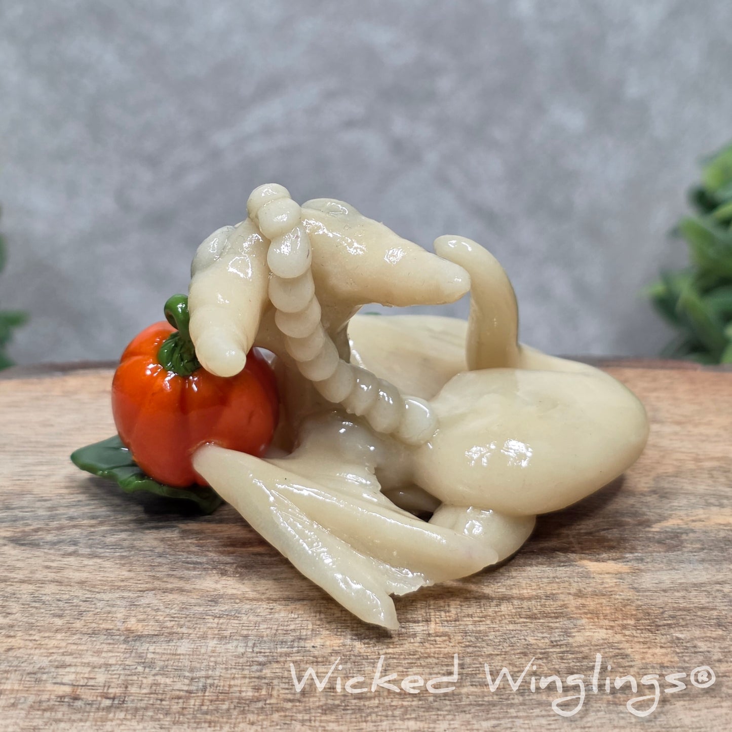 A baby clay dragon sculpture with pumpkins against a wood background with greenery and text Wicked Winglings