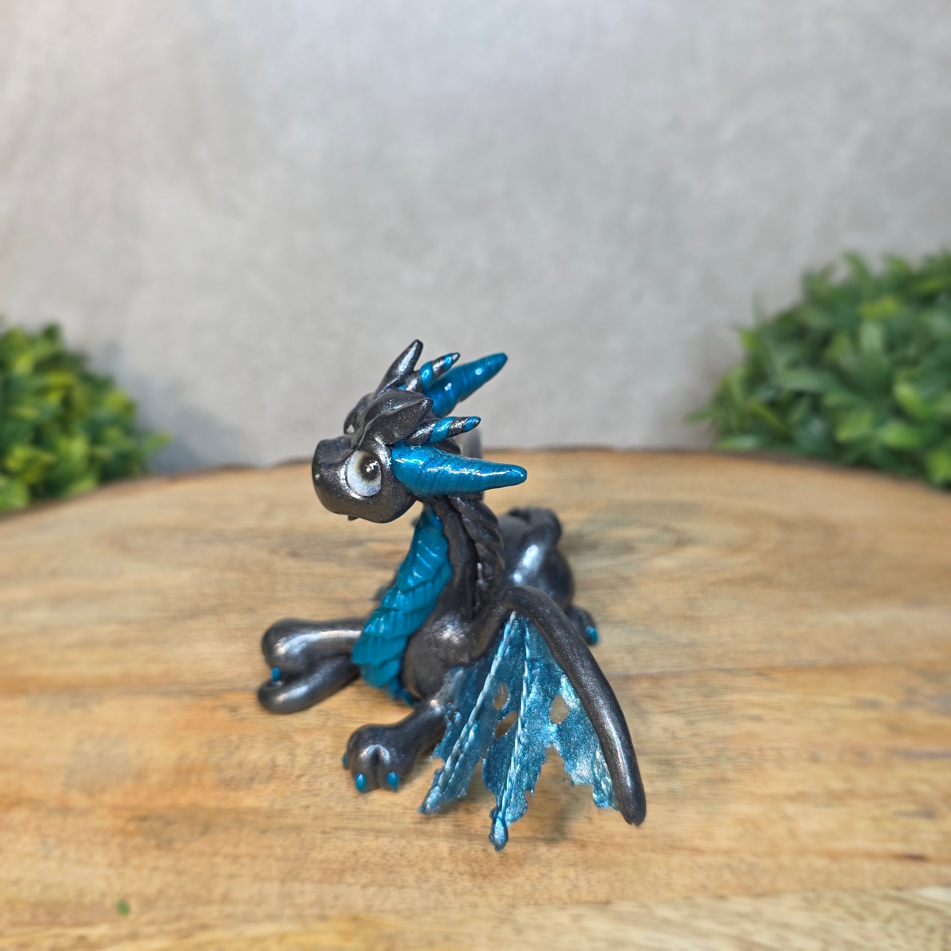 A graphite and blue clay dragon against a blurred wood surface