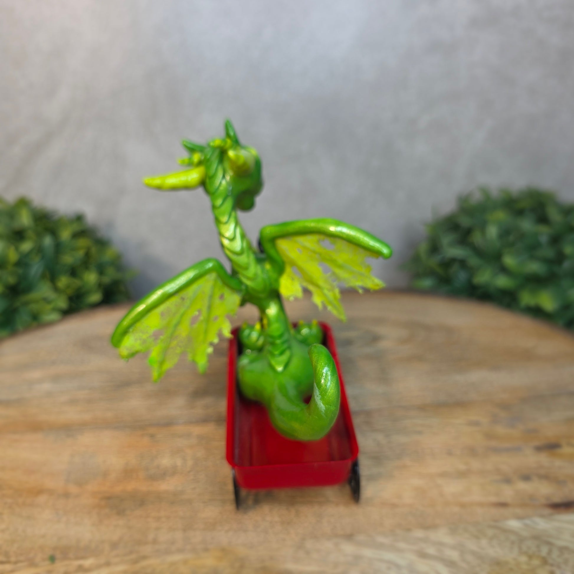 A green clay dragon in a red wagon on a wood surface