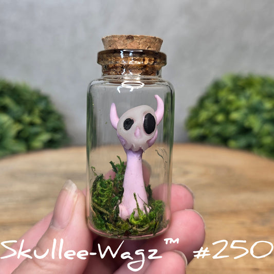 Glass bottle with a skull faced creature and moss, held by a hand with a blurred green background.