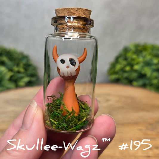 Hand holding a skull faced creature in a jar against a wood background with greenery