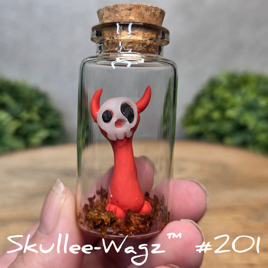 Hand holding a skull faced creature in a jar against a wood background with greenery