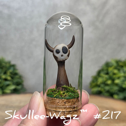 Glass dome with a skull faced creature and moss, held by a hand with a blurred green background.
