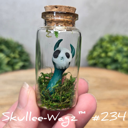 Glass bottle with a skullee-wagz figurine and moss, held by a hand with a blurred green background.