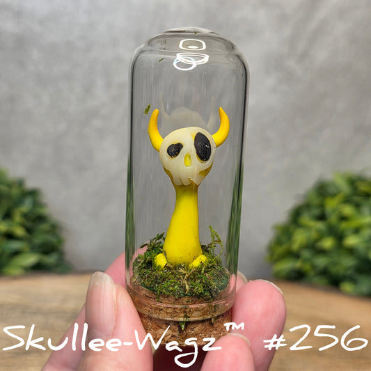 Glass dome with a skull faced creature and moss, held by a hand with a blurred green background.
