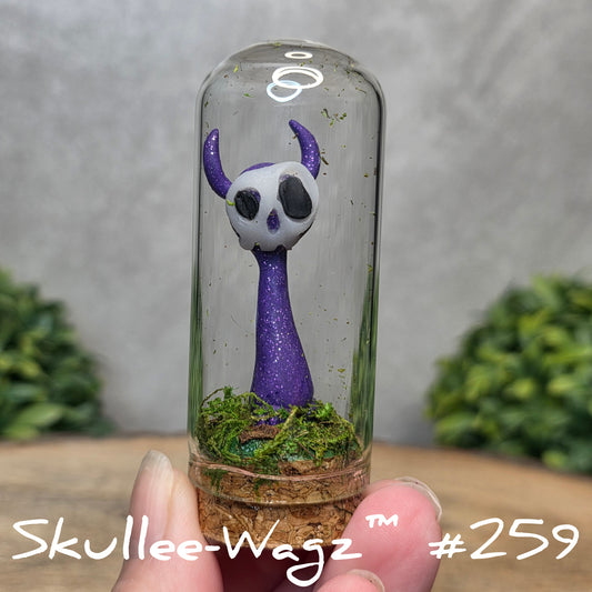Glass dome with a skull faced creature and moss, held by a hand with a blurred green background.