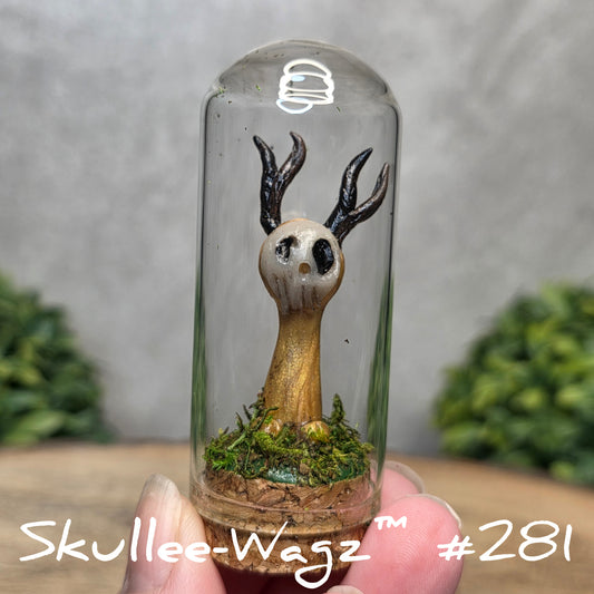 Glass dome with a skull faced creature and moss, held by a hand with a blurred green background.