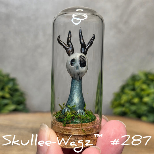 Glass dome with a skull faced creature and moss, held by a hand with a blurred green background.