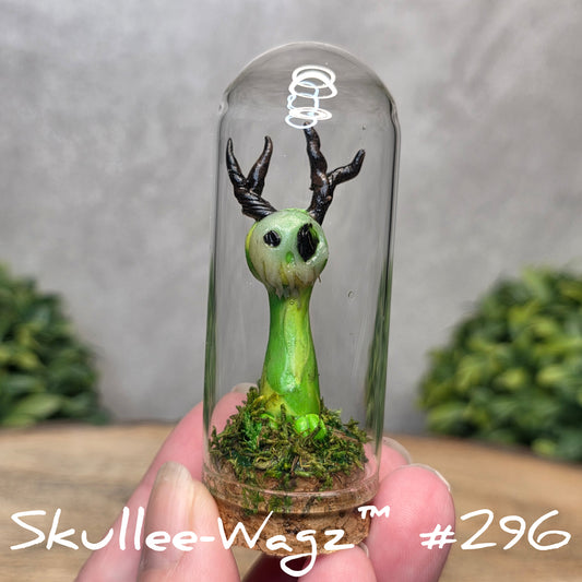 Glass dome with a skull faced creature and moss, held by a hand with a blurred green background.