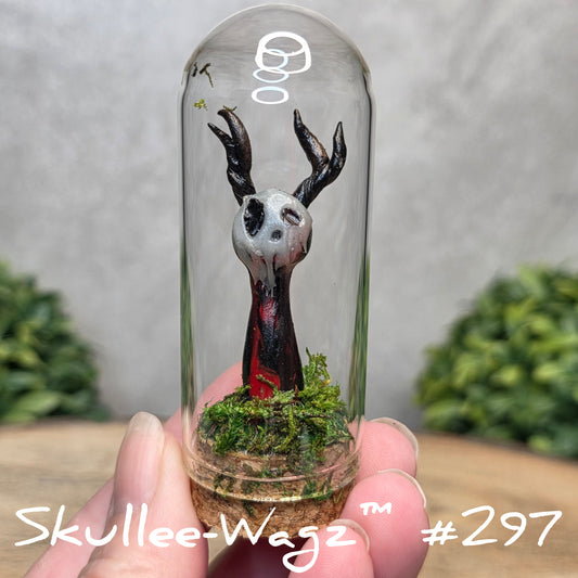 Glass dome with a skull faced creature and moss, held by a hand with a blurred green background.