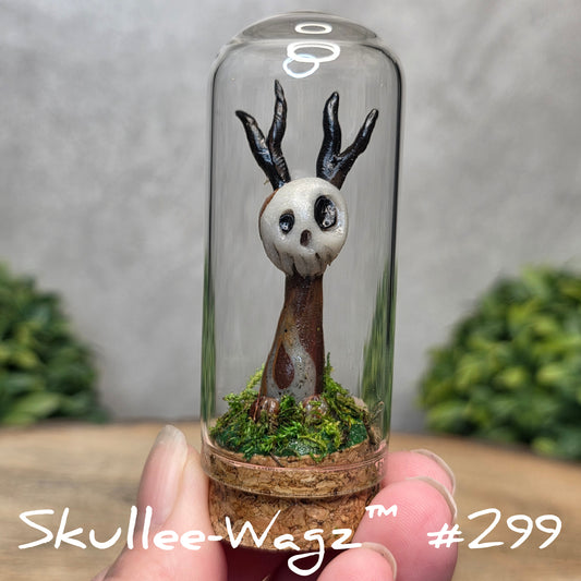 Glass dome with a skull faced creature and moss, held by a hand with a blurred green background.