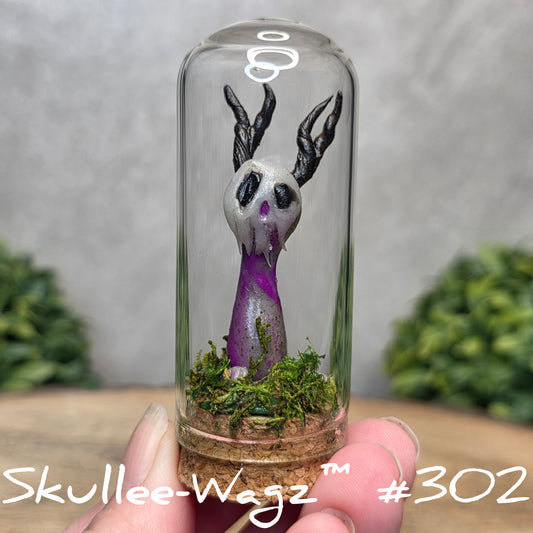 Glass dome with a skull faced creature and moss, held by a hand with a blurred green background.