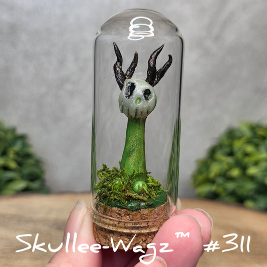 Glass dome with a skull faced creature and moss, held by a hand with a blurred green background.