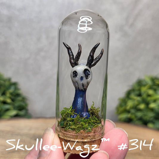 Glass dome with a skull faced creature and moss, held by a hand with a blurred green background.