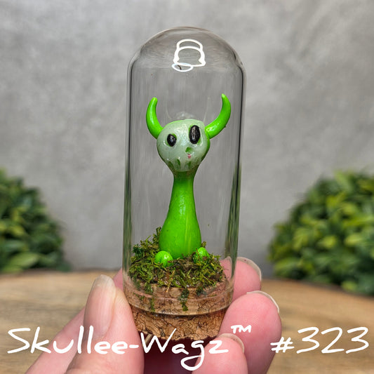 Glass dome with a skull faced creature and moss, held by a hand with a blurred green background.