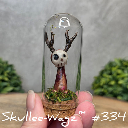 Glass dome with a skull faced creature and moss, held by a hand with a blurred green background.