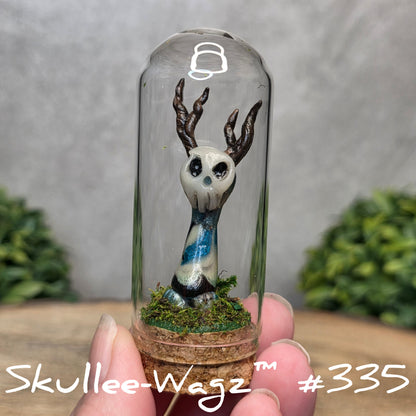 Glass dome with a skull faced creature and moss, held by a hand with a blurred green background.
