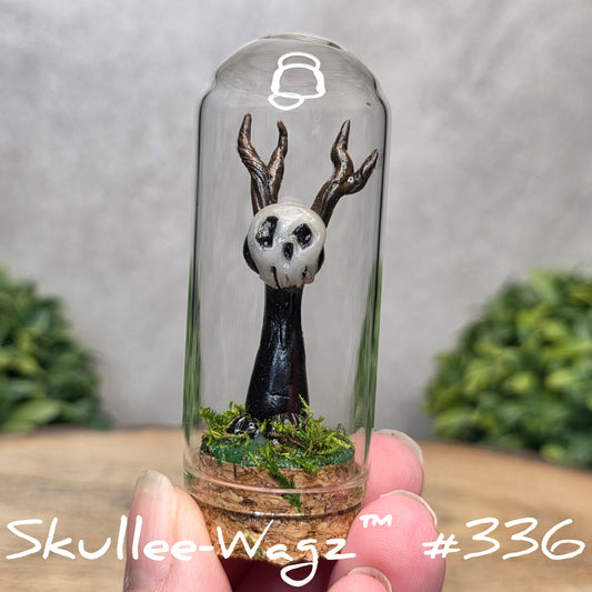 Glass dome with a skull faced creature and moss, held by a hand with a blurred green background.