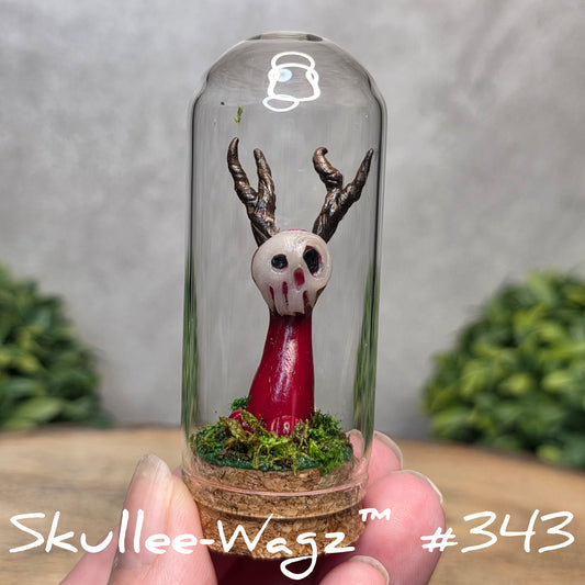 Glass dome with a skull faced creature and moss, held by a hand with a blurred green background.
