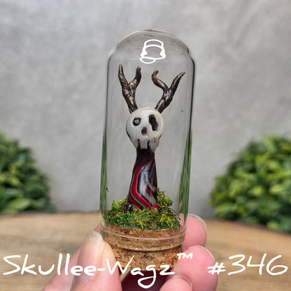 Glass dome with a skull faced creature and moss, held by a hand with a blurred green background.