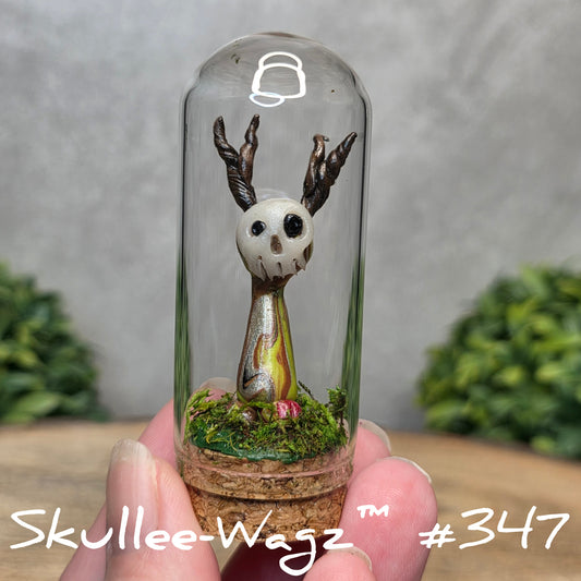 Glass dome with a skull faced creature and moss, held by a hand with a blurred green background.
