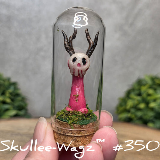 Glass dome with a skull faced creature and moss, held by a hand with a blurred green background.