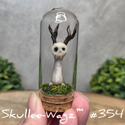 Glass dome with a skull faced creature and moss, held by a hand with a blurred green background.