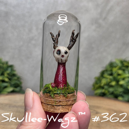Glass dome with a skull faced creature and moss, held by a hand with a blurred green background.