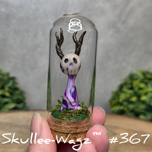 Glass dome with a skull faced creature and moss, held by a hand with a blurred green background.